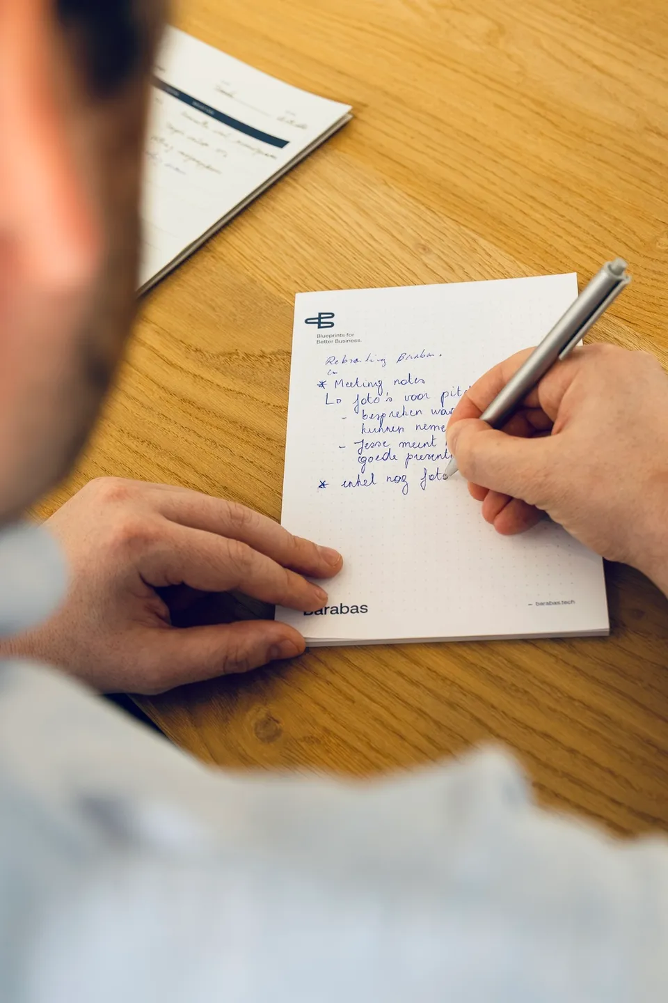 Hand schrijft meeting notes op een Barabas-notitieblok aan de vergadertafel