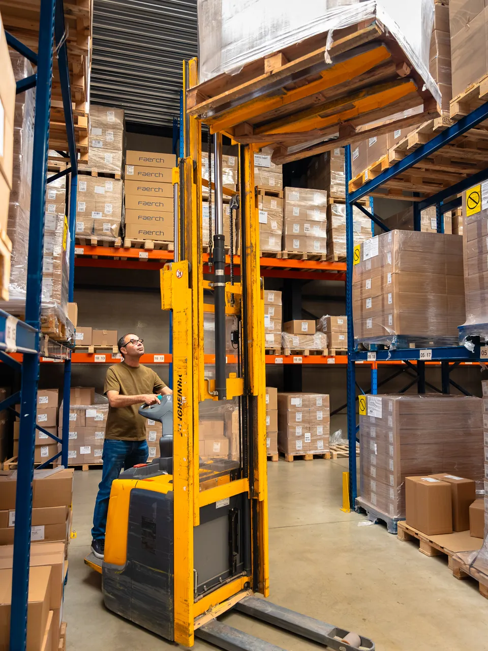 Magazijnier zet met een stapelaar een pallet in het hoogste rek