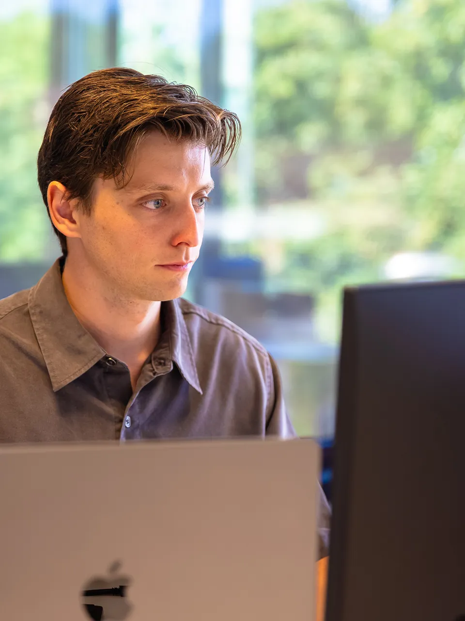 Medewerker aan het werk achter laptop en scherm bij het raam